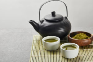 schwarze Teekanne mit Matcha-Pulver auf Bambusmatte